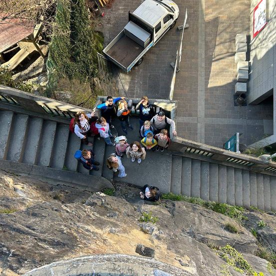 Eine Gruppe von Menschen versammelt sich auf den Stufen einer großen Steinmauer, mit einem geparkten Pickup-Truck in der Nähe.