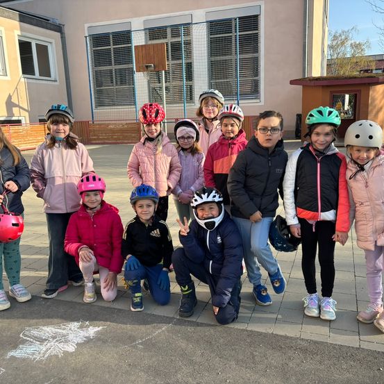 Eine Gruppe von Kindern in Winterkleidung und Helmen posiert für ein Foto vor einem Gebäude. Ein Kreidezeichnung ist auf dem Boden.