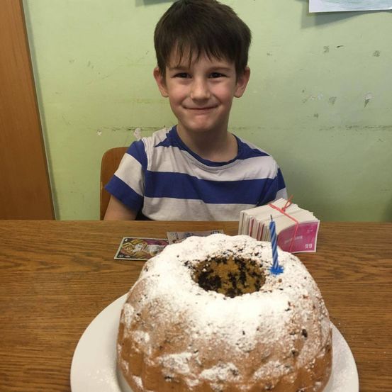 Ein Junge sitzt an einem Tisch mit einem Geburtstagskuchen davor. Der Kuchen hat eine blaue Kerze und ein Loch in der Mitte.