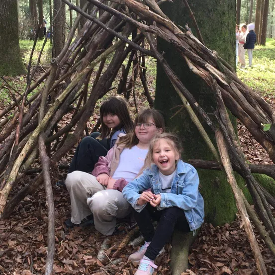 Drei junge Mädchen sitzen in einer Baumhütte aus Ästen im Wald.