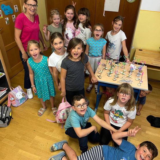 Eine Gruppe von Kindern und einer erwachsenen Frau posieren für ein Foto im Klassenzimmer. Die Kinder lächeln und stehen um einen Tisch mit Dekorationen herum.