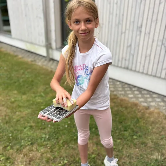 Ein kleines Mädchen reinigt ein Solarpanel mit einem Schwamm, während sie auf einem Rasen steht.