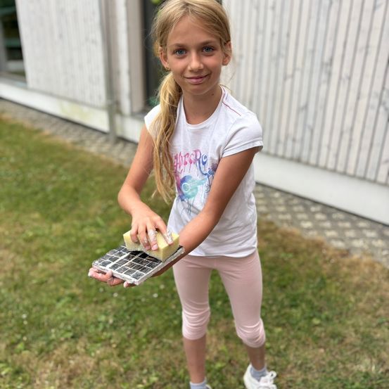 Ein kleines Mädchen reinigt ein Solarpanel mit einem Schwamm, während sie auf einem Rasen steht.
