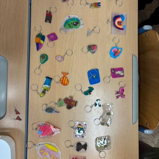 Eine Sammlung von farbenfrohen, handgefertigten Schlüsselanhängern auf einem Holztisch, einschließlich Designs wie Häuser, Regenbögen und Tiere.