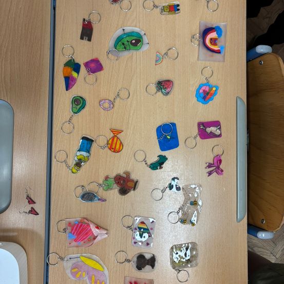 Eine Sammlung von farbenfrohen, handgefertigten Schlüsselanhängern auf einem Holztisch, einschließlich Designs wie Häuser, Regenbögen und Tiere.