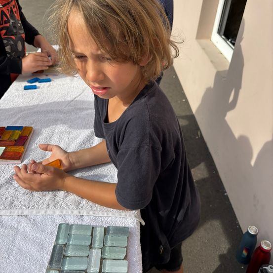 Ein junger Junge konzentriert sich auf ein Bastelprojekt an einem Tisch, umgeben von bunten Fliesen und Materialien.