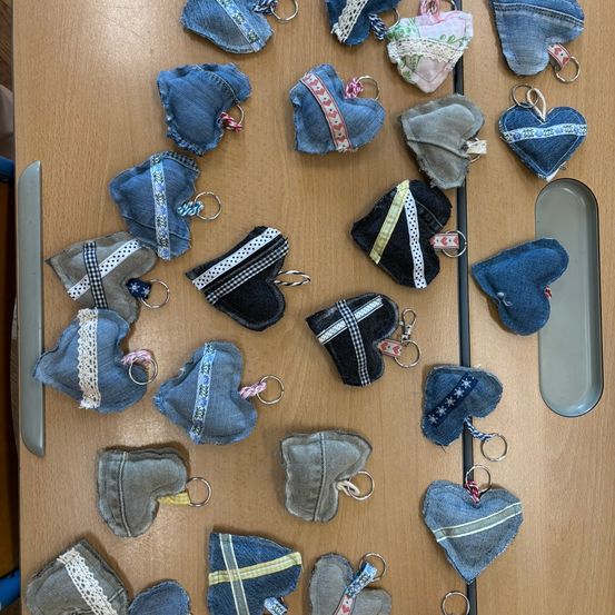 Mehrere denim-herzförmige Schlüsselanhänger sind auf einer Holzoberfläche ausgestellt. Jeder Schlüsselanhänger ist aus Denim-Stoff gefertigt und zeigt verschiedene Designs und Muster. Die Schlüsselanhänger sind in einem Rastermuster angeordnet.