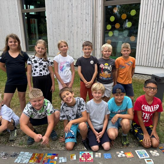 Eine Gruppe junger Kinder posiert für ein Foto vor einem Gebäude mit Mosaikfliesen auf dem Boden.
