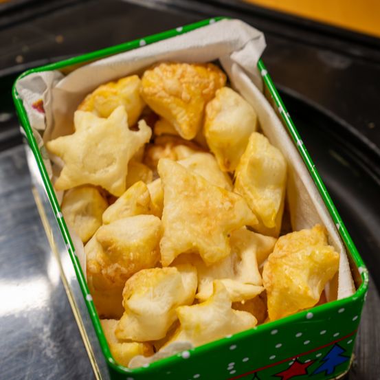 Eine grüne Blechdose mit weißen Punkten enthält goldene, knusprige, sternförmige Snacks, möglicherweise ein festliches Gebäck.