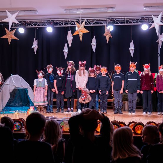 Eine Gruppe von Kindern mit Tiermasken auf der Bühne mit einem Zelt und Sternen im Hintergrund.