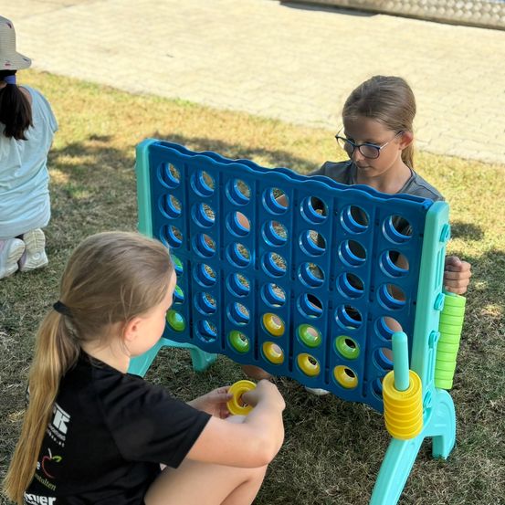 Zwei Mädchen spielen an einem sonnigen Tag Connect Four. Ein Mädchen konzentriert sich auf das Brett, während das andere sich darauf vorbereitet, einen Zug zu machen.