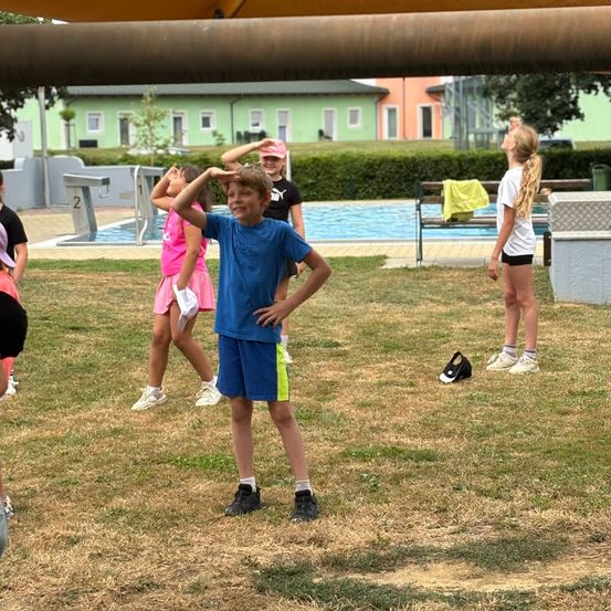 Kinder spielen draußen in der Nähe eines Pools, ein Junge schaut nach oben, während andere zusehen.