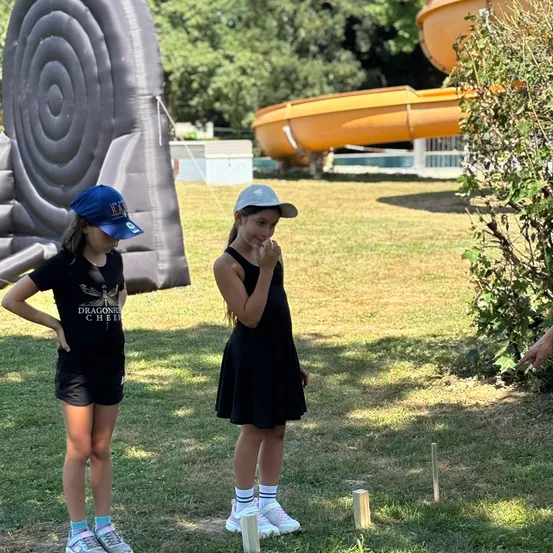 Zwei Mädchen stehen in der Nähe eines Spielplatzes mit einer Rutsche und einer riesigen Schnecke. Ein Mädchen hat eine Kappe, und das andere hat ein Kleid. Sie scheinen ein Spiel zu spielen.