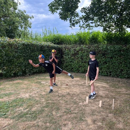 Drei Jungen spielen ein Spiel Kegeln im Garten hinter einem Busch. Ein Junge bereitet sich darauf vor, einen Ball zu werfen.