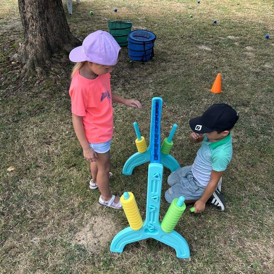Zwei Kinder spielen mit einem blauen und gelben Spiel, indem sie gelbe Bälle durch die Löcher rollen.