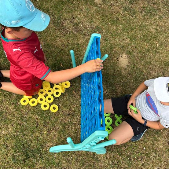 Zwei Kinder spielen auf dem Rasen. Ein Kind hält einen gelben Ring und platziert ihn auf einem blauen Brett. Das andere Kind hält einen grünen Ring.