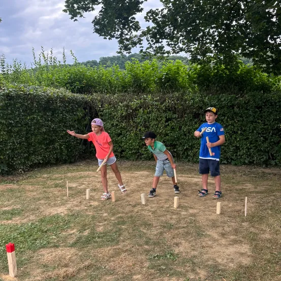 Drei Kinder spielen an einem sonnigen Tag ein Spiel Outdoor-Croquet und stehen in einem Kreis aus Holzstöcken.
