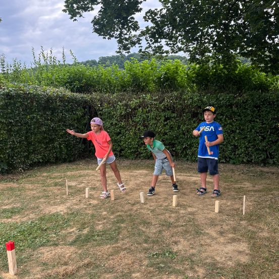 Drei Kinder spielen an einem sonnigen Tag ein Spiel Outdoor-Croquet und stehen in einem Kreis aus Holzstöcken.