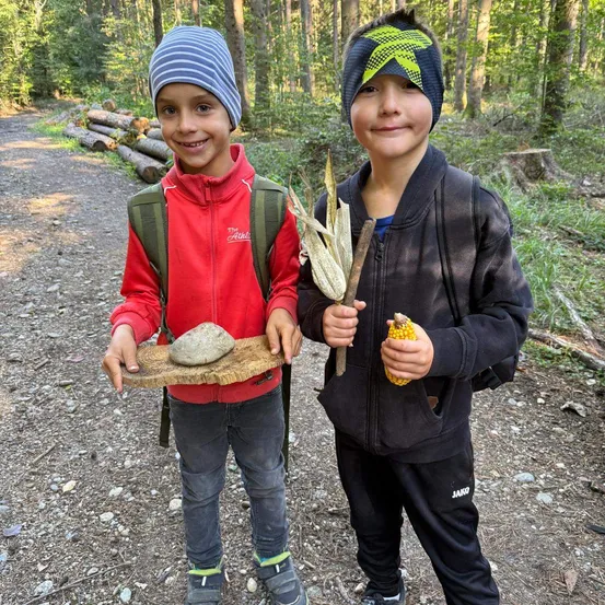Zwei junge Jungen im Wald, einer hält einen Stein und der andere einen Maiskolben und einen Stock.