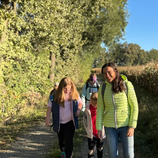 Eine Gruppe von Kindern und Erwachsenen geht auf einem Kiesweg, umgeben von Bäumen und Gras.