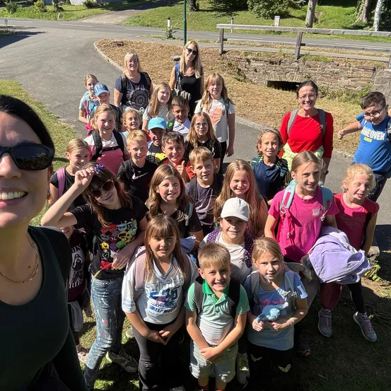 Eine Gruppe von Kindern und Erwachsenen, einschließlich Lehrerinnen, stehen zusammen auf einem Rasen und lächeln für ein Foto.