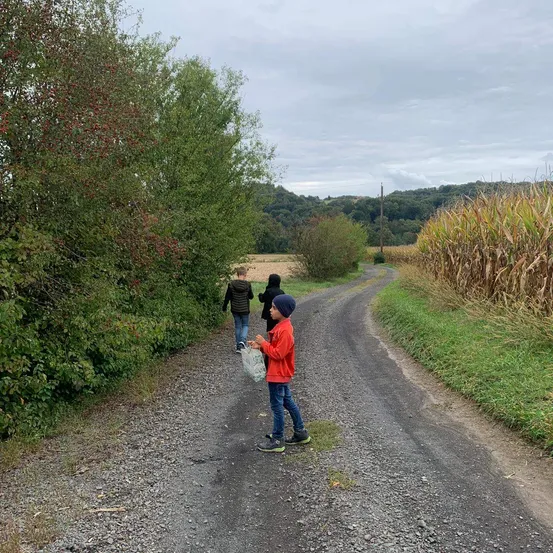 Drei Kinder gehen einen Schotterweg entlang, mit einem Maisfeld auf der rechten Seite.