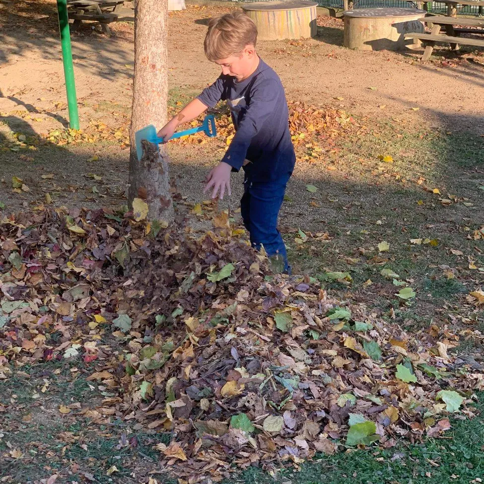 Ein junger Junge fegt Blätter in einem Park.