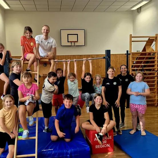 Eine Gruppe von Kindern und Erwachsenen ist in einem Fitnessstudio. Einige Kinder sind auf einer Leiter und andere an einem Barren.