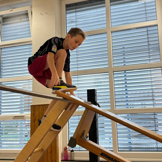 Ein junger Junge balanciert auf einer hölzernen Rampe in einer Turnhalle.
