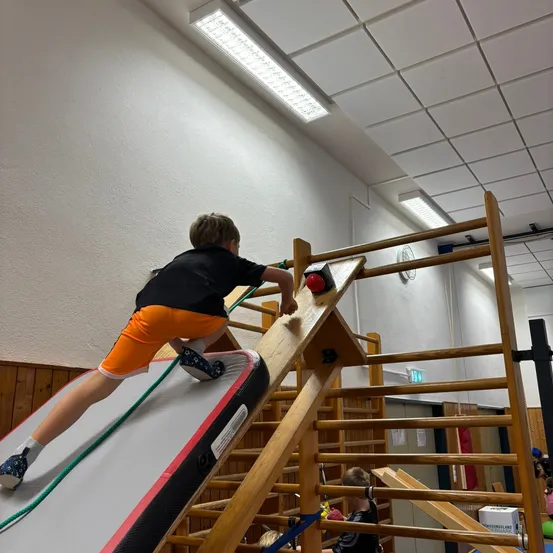 Ein junger Junge klettert auf eine Holzstruktur mit einem roten Knopf an der Spitze.