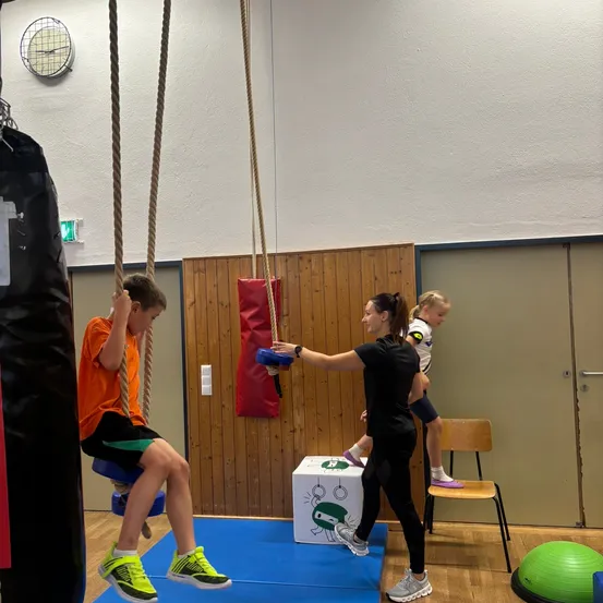 Eine Frau hilft einem Jungen, in einem Fitnessstudio eine Seil zu erklimmen.