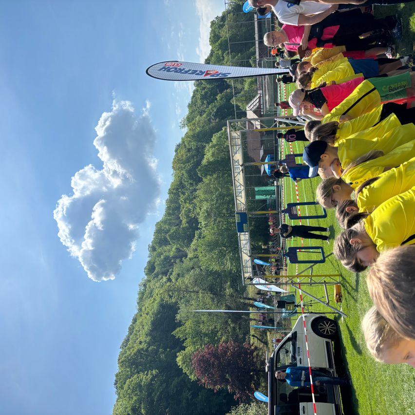 Eine Gruppe von Menschen in gelben Shirts wartet in einer Schlange unter einem Himmel mit einer flauschigen Wolke.