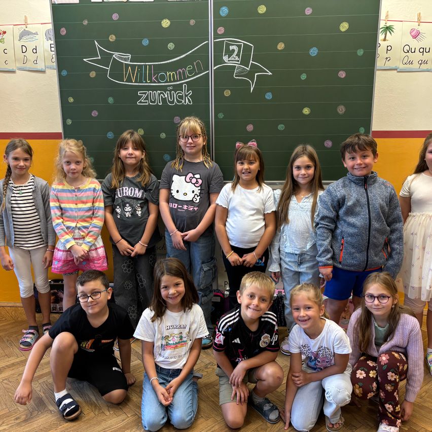 Eine Gruppe von Kindern posiert für ein Foto in einem Klassenzimmer mit einer Tafel, auf der Willkommen zuruck steht.