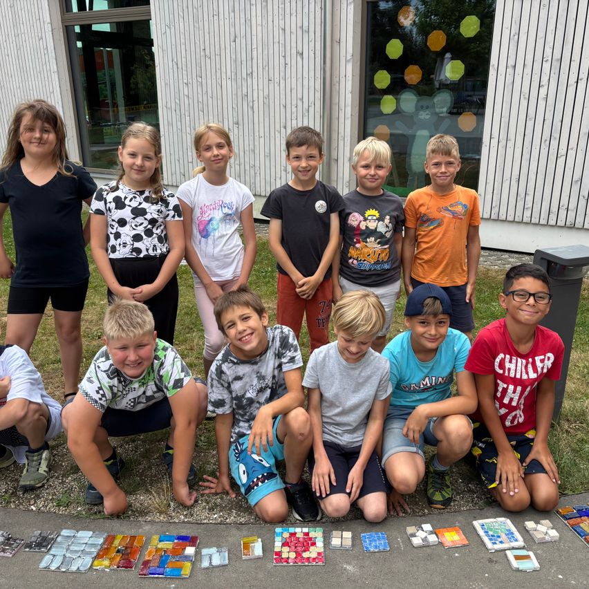 Eine Gruppe von Kindern posiert vor einem Gebäude mit bunten Fliesen auf dem Boden, lächelt und schaut zur Kamera.