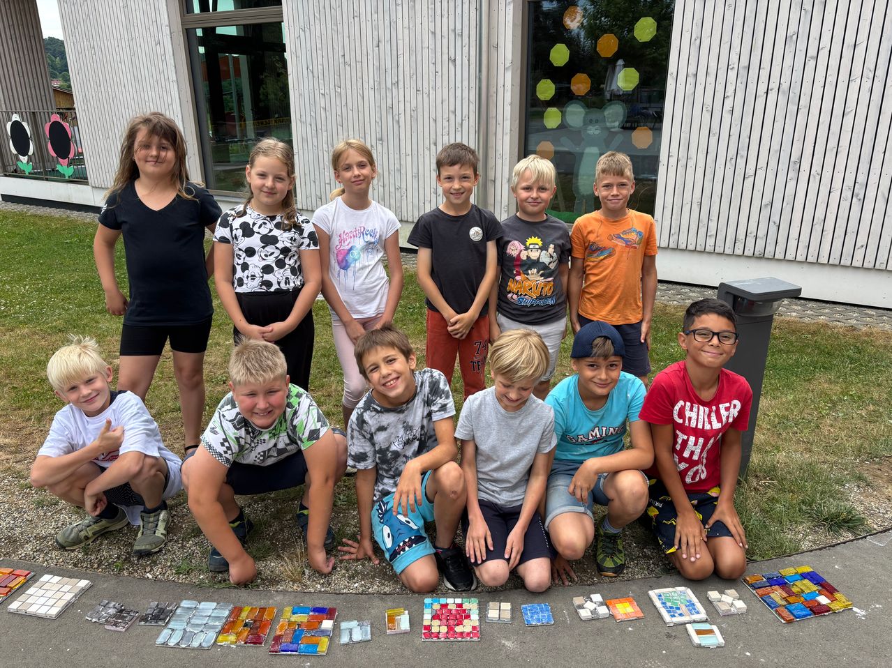 Eine Gruppe von Kindern posiert vor einem Gebäude mit bunten Fliesen auf dem Boden, lächelt und schaut zur Kamera.