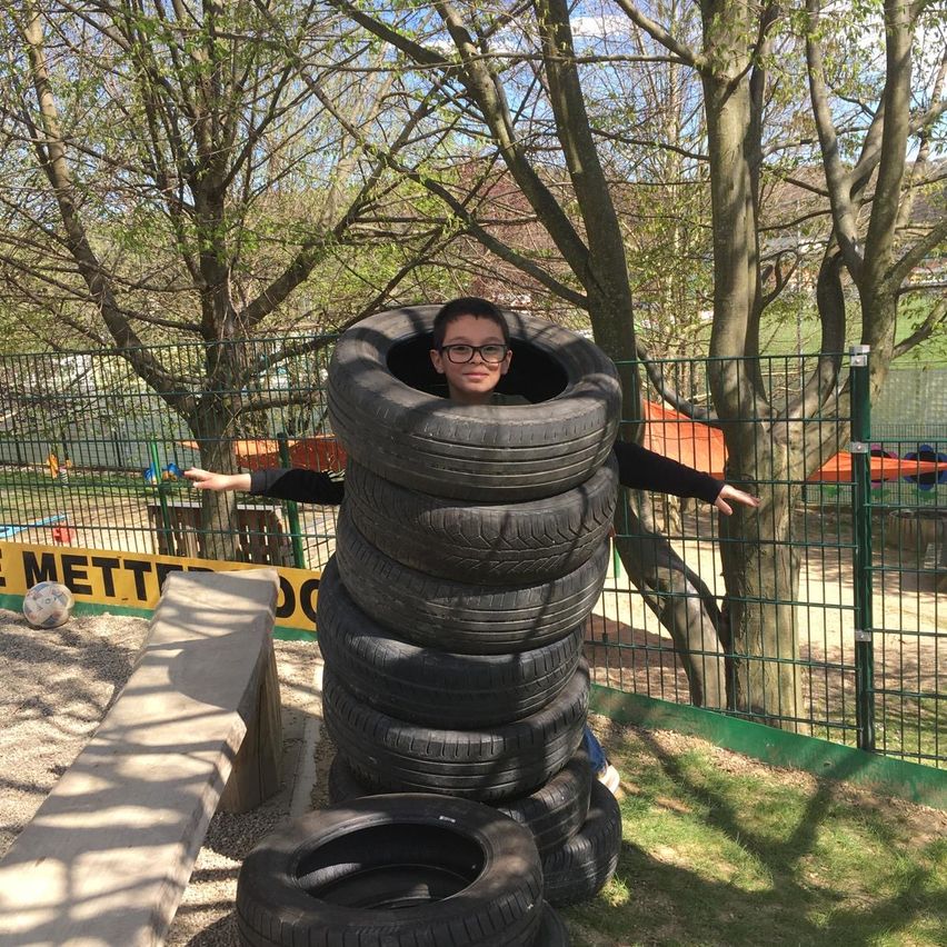 Ein junger Junge steht in einem Reifenstapel im Spielplatz, neben einem Fußball und einer Bank.