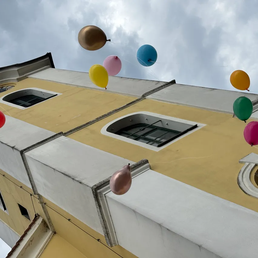 Eine bunte Reihe von Ballons schwebt über einem gelben und weißen Gebäude mit Bogenfenstern.