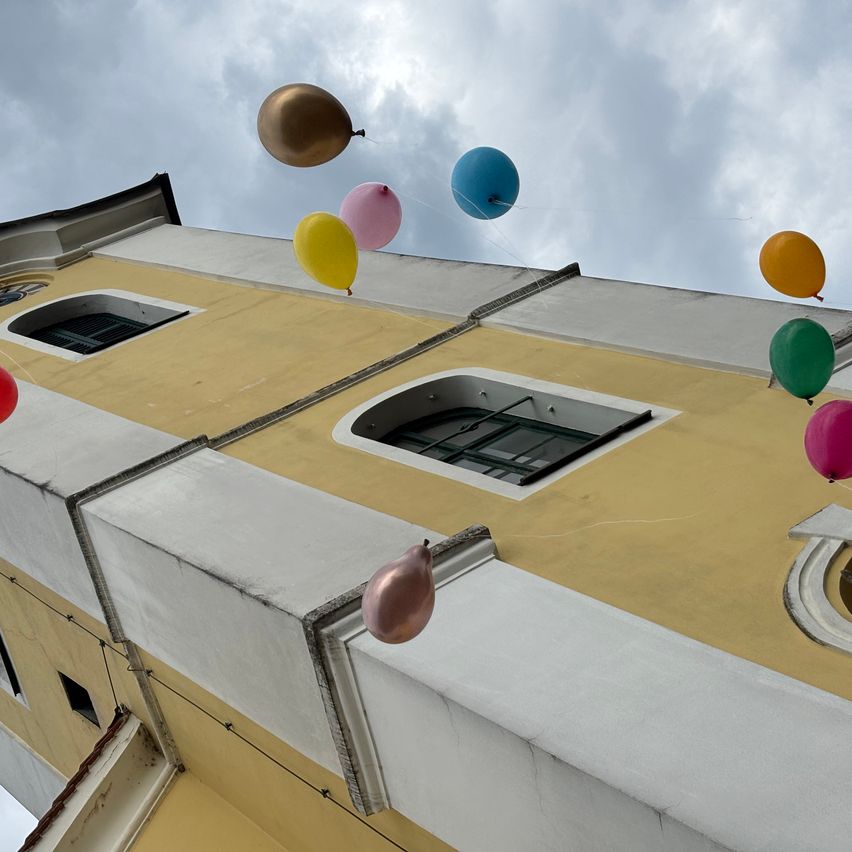 Eine bunte Reihe von Ballons schwebt über einem gelben und weißen Gebäude mit Bogenfenstern.