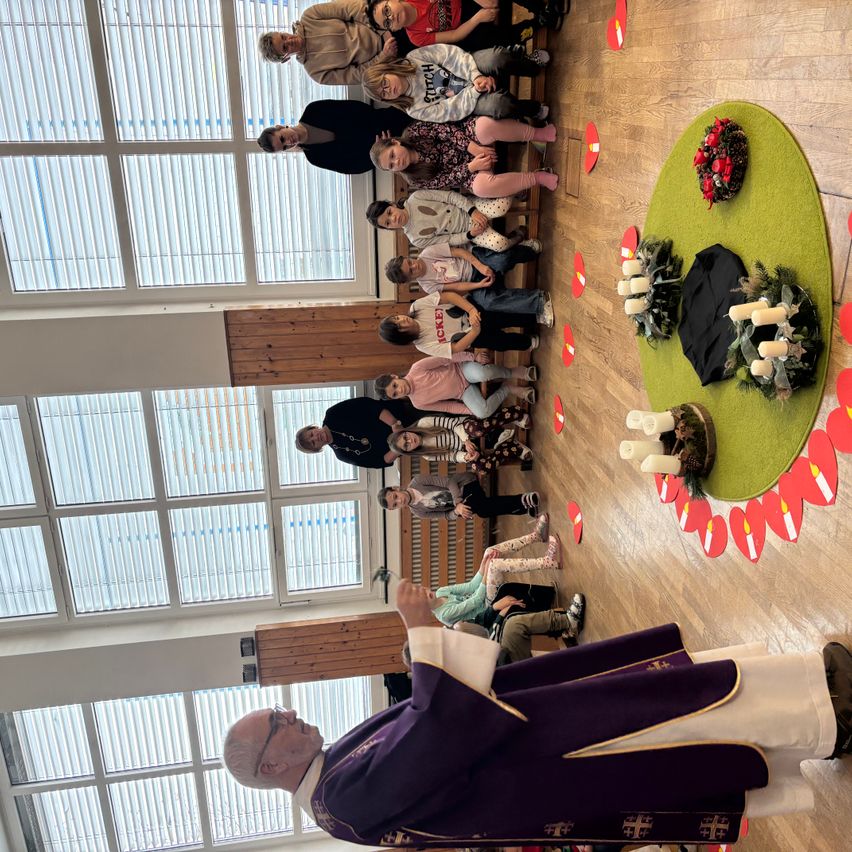 Ein Priester leitet eine Zeremonie in einer Kirche. Die Menschen sitzen auf dem Boden und um einen geschmückten Altar herum. Kerzen sind um den Altar herum platziert.