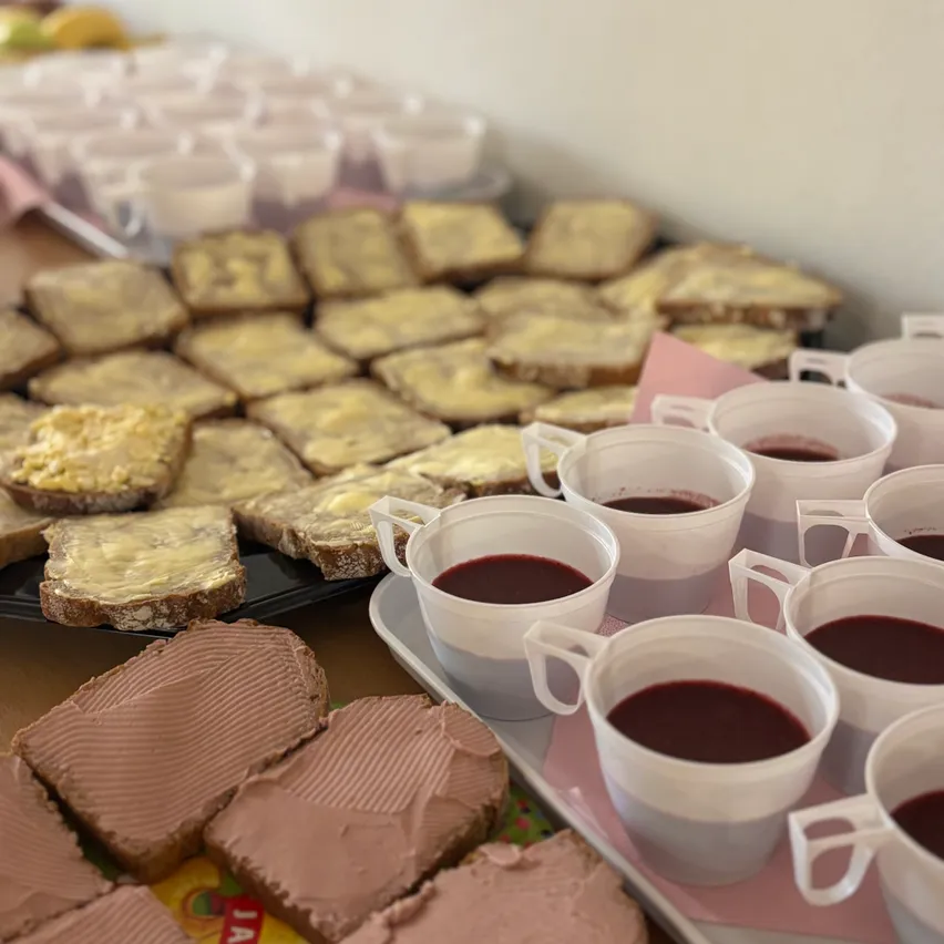 Ein Tisch ist gedeckt mit Sandwiches mit Butter und Schokoladenaufstrich, zusammen mit Tassen gefüllt mit roter Flüssigkeit.