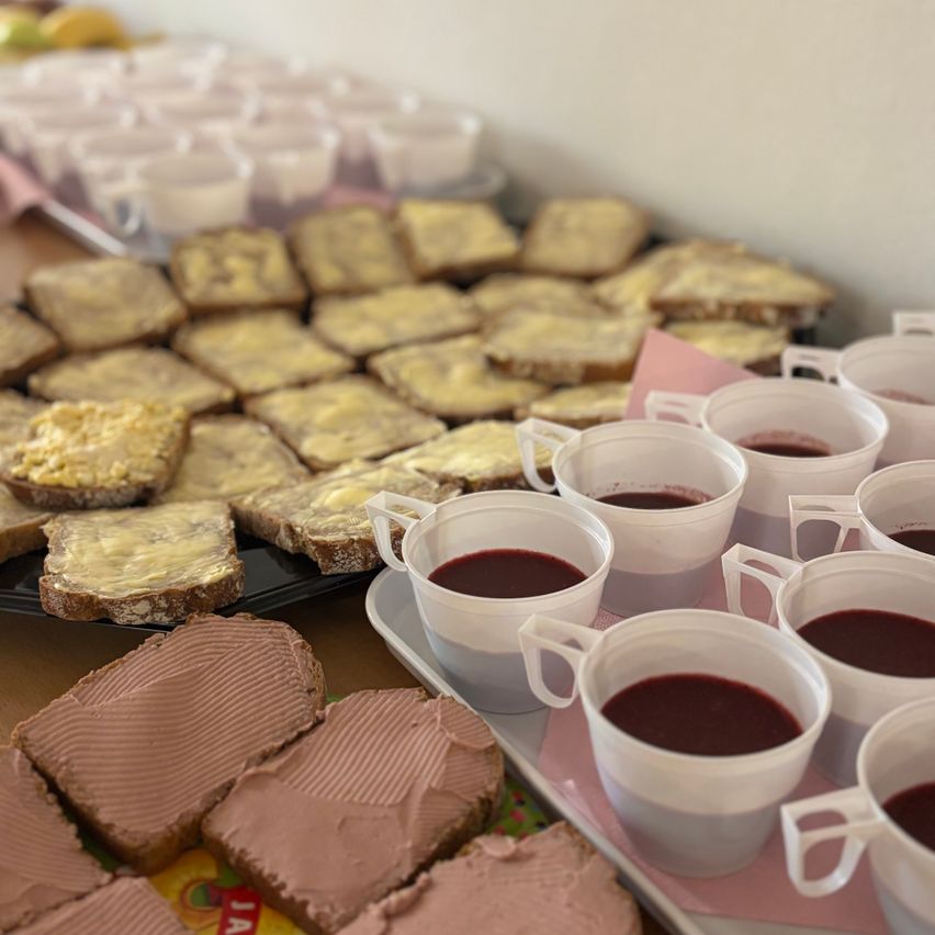 Ein Tisch ist gedeckt mit Sandwiches mit Butter und Schokoladenaufstrich, zusammen mit Tassen gefüllt mit roter Flüssigkeit.