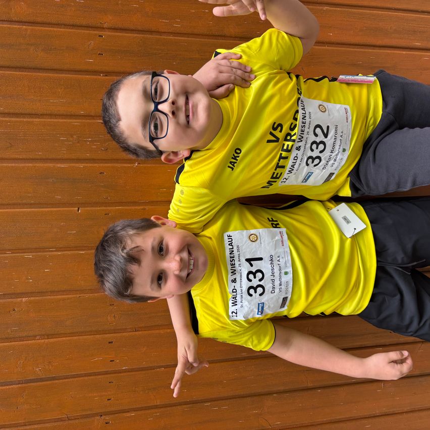 Zwei Jungen, die gelbe T-Shirts mit den Nummern 331 und 332 tragen, lächeln und posieren für ein Foto.