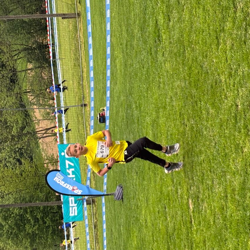 Ein Läufer mit gelbem Trikot und der Nummer 679 befindet sich mitten in einem Rennen auf einem Rasenfeld.