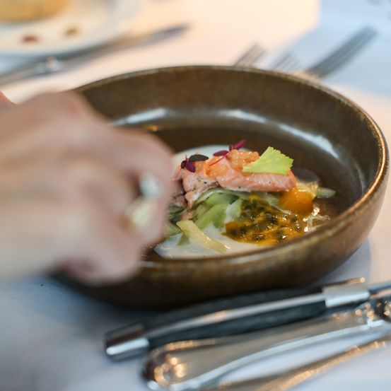 Eine Person garniert eine Schüssel mit Lachs und Zitrone mit Kräutern. Ein Teller, Messer und Gabel sind in der Nähe.