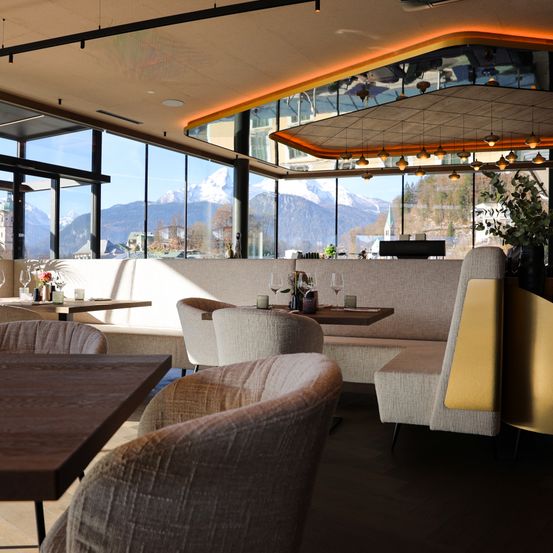 Ein modernes Restaurant mit großen Fenstern und Bergblick. Es gibt Tische mit Stühlen und dekorative Gegenstände auf den Tischen.