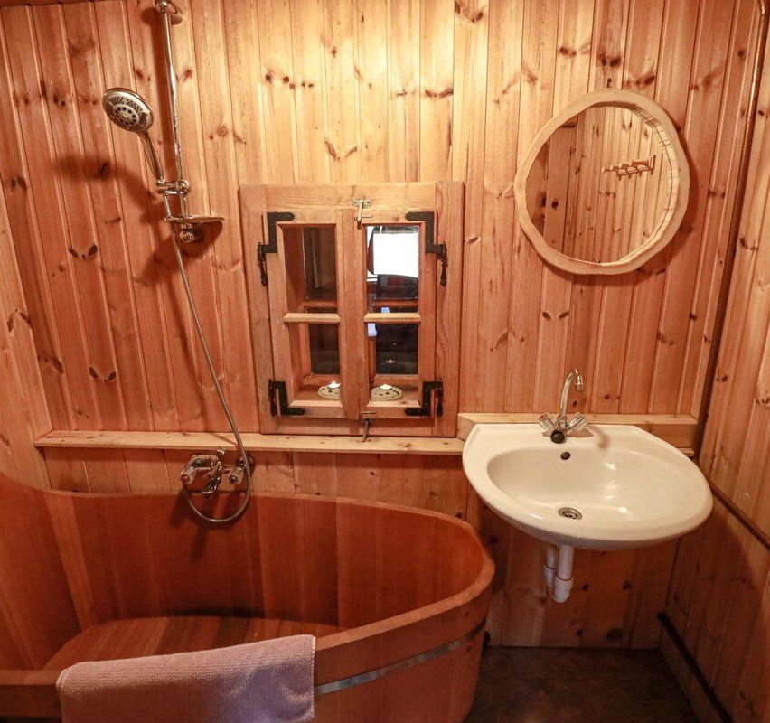 A bathroom with wooden walls, a bathtub, a sink, a mirror, and a window with a view outside.