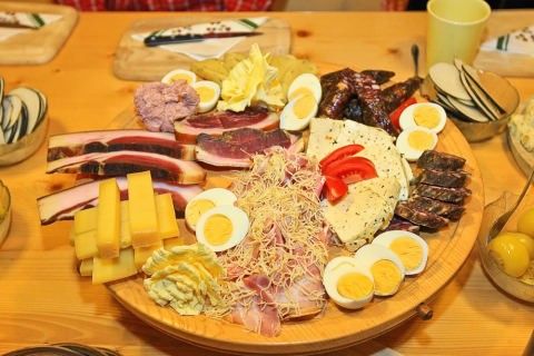 A large round platter on a wooden table is filled with various meats, eggs, cheese, and vegetables. There are also bowls of sliced vegetables.