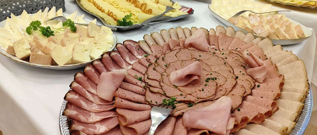 Ein Tisch mit verschiedenen Platten von Fleisch und Käse. Schinken, Käse und geschnittenes Fleisch sind prominent ausgestellt.