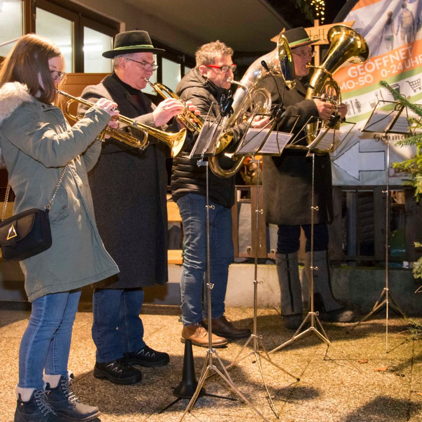 Eine Gruppe von Musikern spielt Instrumente, darunter Trompeten und Tubas, in einem Außenbereich bei Nacht.