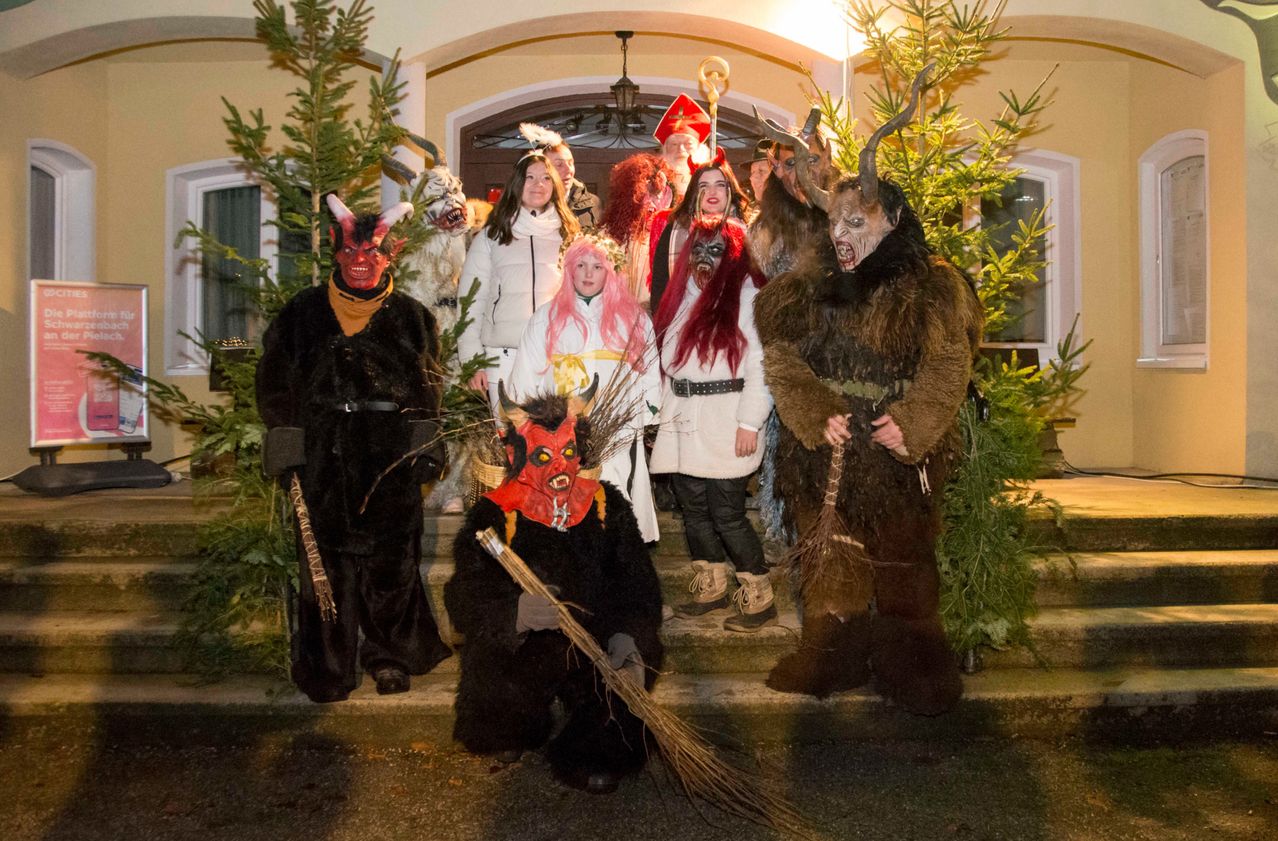 Eine Gruppe von Menschen in aufwendigen Kostümen, möglicherweise für ein Festival, steht bei Nacht vor einem Gebäude.